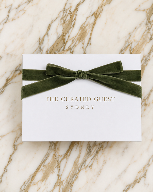 White gift boxwith sage green velvet bow and 'The Curated Guest Sydney' text on a marble background