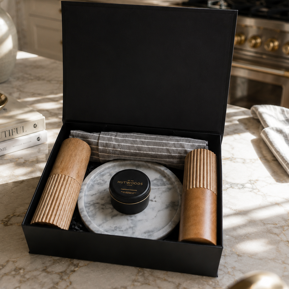 Gift box with marble tray, wooden items, and black container in a black box on a marble surface.