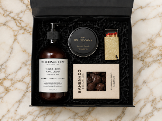 Gift set with Murchison & Hume velvet glove hand cream, Hutwoods travel candle, and Bahen & Co chocolate truffles on a marble surface.